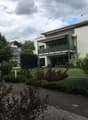 Modern two-story house with white exterior, large windows, balcony, and well-maintained garden.