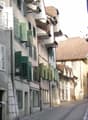 A narrow cobblestone street lined with multi-story buildings featuring green shutters and classic architectural details.