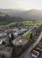 Aerial view of a suburban neighborhood with residential buildings, roads, and surrounding green fields and hills.
