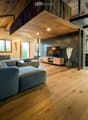 Modern living room with wooden floors, exposed wooden beams, large windows, sectional sofa, coffee table, TV, and decorative vase.