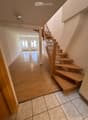 Spacious hallway with wooden flooring, a staircase with wooden steps and a metal railing, and a view into an adjacent room with large windows and a radiator.