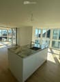 Modern kitchen with light wooden flooring, white cabinets, marble countertop, and large windows offering a view of the city.