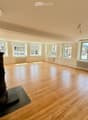 Empty room with wooden flooring, large windows, and a central heating stove. No furniture or equipment present.