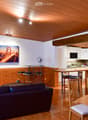 Open living room, sofa, wooden dining table, kitchen island, dining chairs, TV, painting on wall, ceiling light, fan