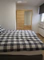 Cozy bedroom with a wooden bed, checkered bedding, a wooden wardrobe with a mirror, and a landscape painting on the wall.