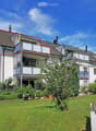 Modern multi-story residential building with balconies, surrounded by a well-maintained lawn and garden area.
