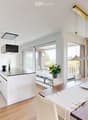 Modern open-plan kitchen and dining area with white cabinets, a central island, pendant lights, and large windows overlooking a balcony.