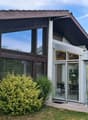 Modern two-story house with large windows, sliding glass doors, and a well-maintained garden with potted plants.