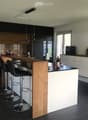 Modern kitchen with dark cabinets, wooden island, black stools, and pendant lights.