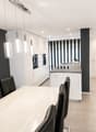 Modern kitchen and dining area with white cabinets, a central island, pendant lights, and a dining table with black chairs.