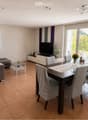 Modern living and dining area with a brown sectional sofa, glass coffee table, dark wooden dining table with four chairs, flat-screen TV on a white stand, and decorative vases on the table and TV stand.