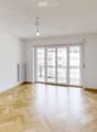 Empty room with wooden herringbone flooring, white walls, and large sliding glass doors leading to a balcony.