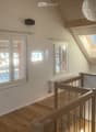 Bright hallway with wooden flooring, white walls, multiple windows including a skylight, and a wooden staircase railing.