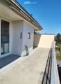 Balcony with concrete floor, glass sliding doors, metal railing, and a view of greenery and trees.
