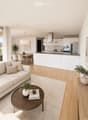 Open-plan living and dining area with a light-colored sofa, coffee table, dining table, and modern kitchen featuring white cabinets and stainless steel appliances.