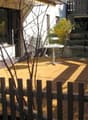 Wooden deck with a small round table, surrounded by a wooden fence, with a view of the house and garden.