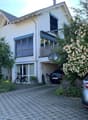 Two-story house with white exterior, garage, balcony, and driveway with parked cars.