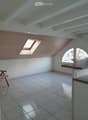 Bright, airy attic room with wooden slatted walls, skylight windows, tiled floor, and a single wooden chair near the wall.