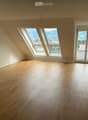 Empty room with wooden flooring, large windows, and a sliding glass door leading to a balcony.