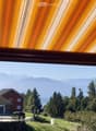 Balcony with a view of a house, trees, and mountains in the background.