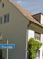 white house, brown roof, windows, balcony, green plants, sign