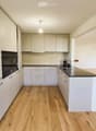 Modern kitchen with white cabinets, black countertops, and wooden floors.