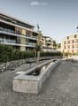 Modern multi-story residential buildings with balconies and contemporary design, surrounded by greenery and a paved walkway.