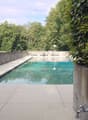 Outdoor swimming pool area with concrete walls, tiled deck, and surrounding greenery.