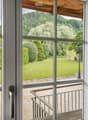 Balcony with wooden decking, metal railing, and scenic view of a green lawn, trees, and hills.