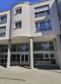 Modern building with a curved facade, large glass windows, and a raised ground floor supported by concrete pillars.