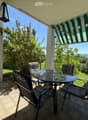 Balcony with a glass table and four chairs, overlooking a green landscape with trees and hills.