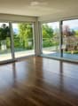 Empty room with wooden flooring and large sliding glass doors leading to a balcony with a scenic view of trees and mountains.