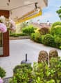 Well-maintained garden with lush greenery, flowering shrubs, decorative statues, and a covered patio area with a glass door leading inside.