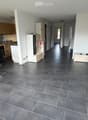 Open-plan living and dining area with grey tiled flooring, modern kitchen area with cabinets and appliances, and a dining table with chairs.