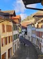 A narrow cobblestone street lined with colorful, multi-story buildings with traditional European architecture, featuring wooden shutters and tiled roofs.