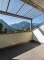 Balcony with tiled floor, glass roof, and scenic mountain view.