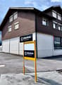 Two-story building with brown wooden facade, multiple windows, and signage for "bikebox.ch" and "SCHMERIKON" on the walls. A yellow signpost in front displays the address "Hantteilstrasse 2".
