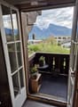 Balcony with a scenic mountain view, featuring a small round table, two flower pots, a wooden stool, and decorative vases.