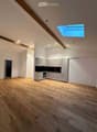 Empty room with wooden flooring, white walls, and a small kitchen area with cabinets and appliances.