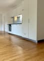 Empty room with light wooden flooring and white kitchen cabinets, no furniture or appliances present.