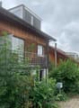 Two-story wooden building with a flat roof and balcony, surrounded by greenery.