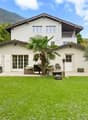 Two-story white house with a balcony, surrounded by a well-maintained lawn, palm tree, and outdoor seating area.