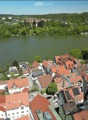 Aerial view of a town with numerous houses, red-tiled roofs, and a lake in the background.