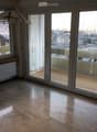 Empty room with large sliding glass doors leading to a balcony, polished stone floor, radiator, and a view of the city and mountains.