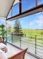 Spacious balcony with large glass windows offering a scenic countryside view, featuring a wooden sofa and a potted plant.