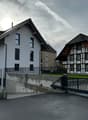 Two-story house with white exterior and multiple windows, adjacent to a traditional half-timbered house with a sloped roof.