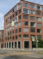 modern multi-story building, brick facade, glass windows, balconies, ground-level storefronts, overhead power lines