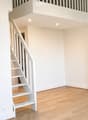 Empty room with light wooden flooring and white walls, featuring a white staircase leading to an upper level.