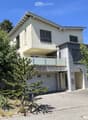Modern two-story house with a garage, balcony, and contemporary design, surrounded by greenery.