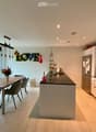 Modern kitchen with white cabinets, a central island, a dining table with chairs, and a vase of flowers. The space features recessed lighting and a pendant light above the island.